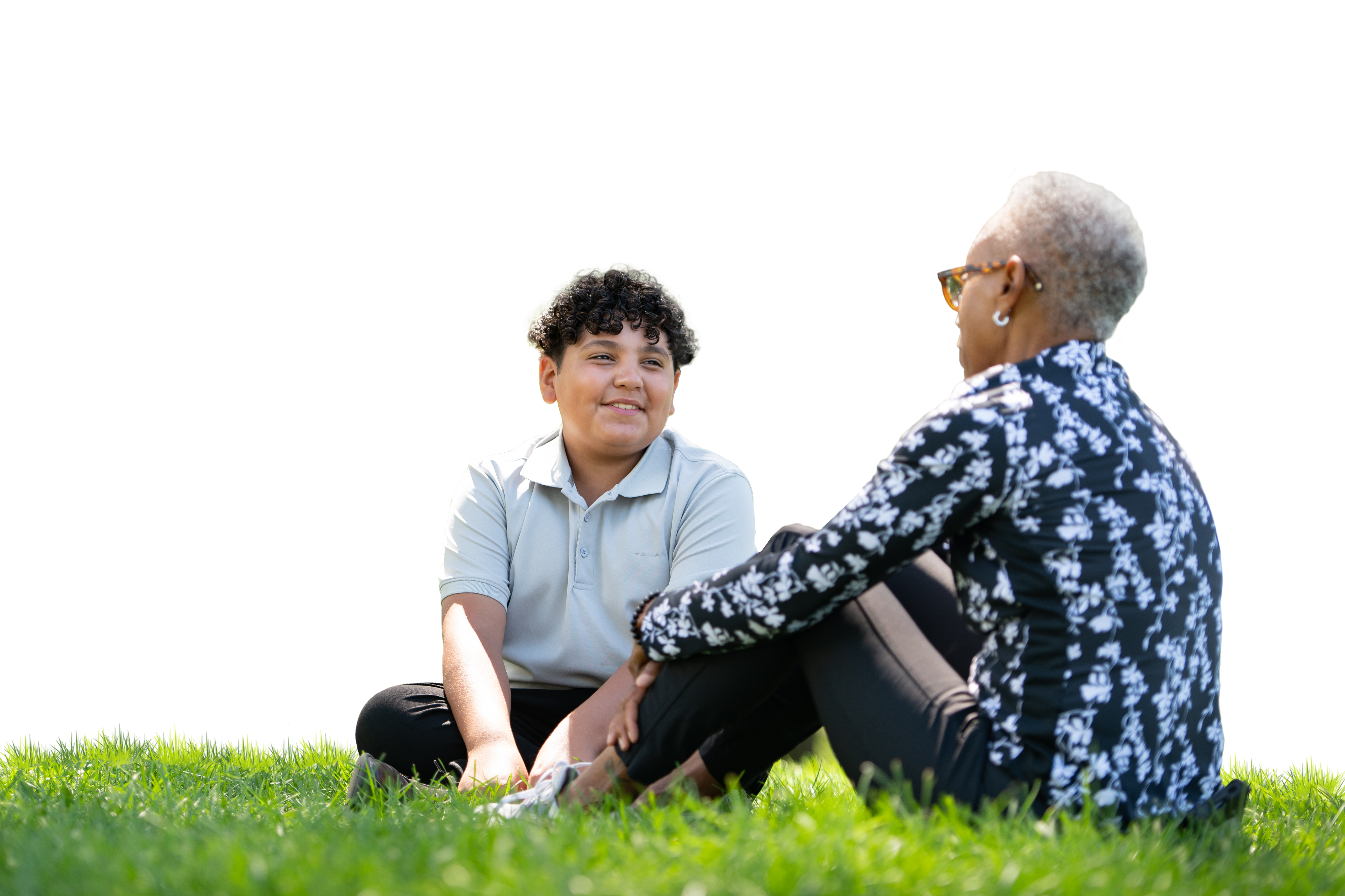 Volunteer sits talking with boy on grass